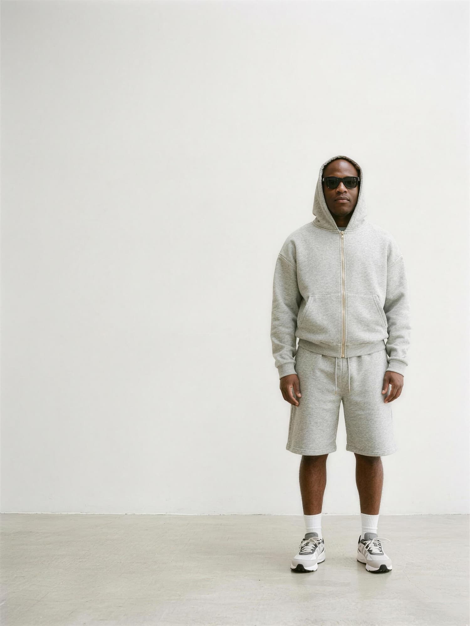 A model wearing the Kensington Zip Hoodie in grey marl with the hood up and matching shorts, standing against a plain studio wall.